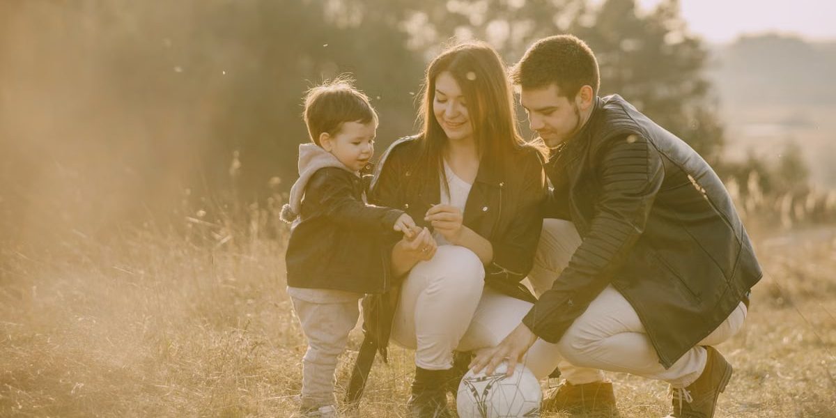 A cheerful family bonding outdoors with a soccer ball, enjoying a sunny day in the grass.
