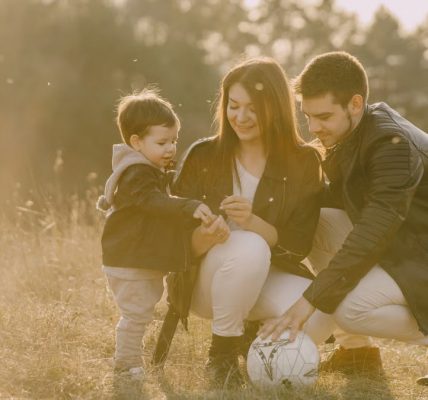 A cheerful family bonding outdoors with a soccer ball, enjoying a sunny day in the grass.