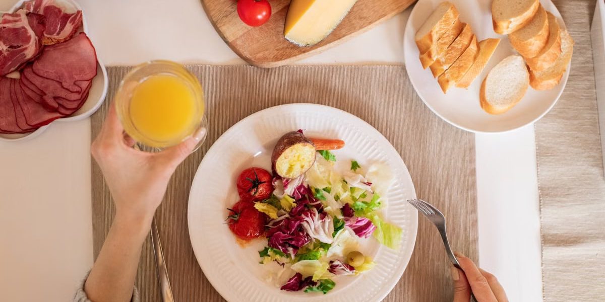 A top-view of a delicious breakfast setting featuring a salad, bread, cheese, tomatoes, and orange juice.