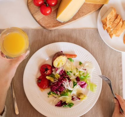 A top-view of a delicious breakfast setting featuring a salad, bread, cheese, tomatoes, and orange juice.