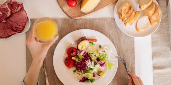 A top-view of a delicious breakfast setting featuring a salad, bread, cheese, tomatoes, and orange juice.